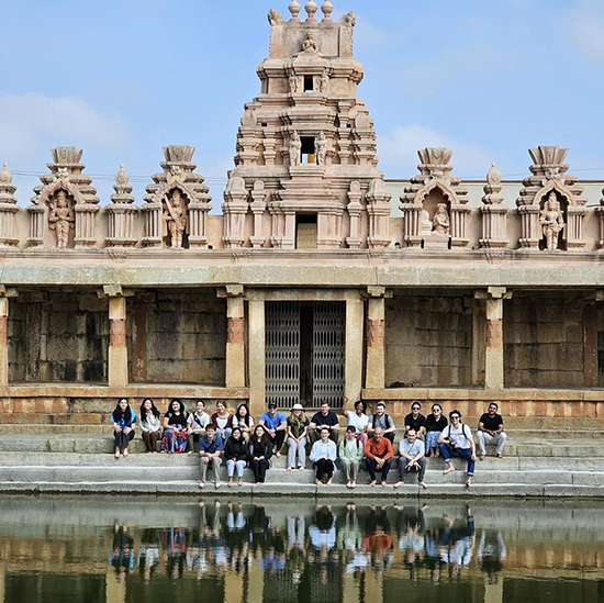 A group of students sit on steps in front of a stone temple in Bangalore, India.