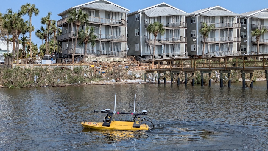 A yellow aquatic drone on a body of water with residential buildings and palm trees in the background.