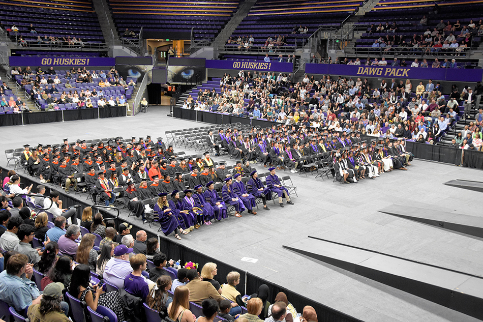 Wide view of the graduation ceremony with audience, graduates and faculty in an arena.
