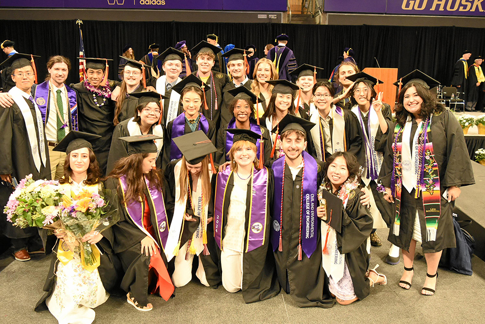 Large group of graduates posing together on stage in their gowns.