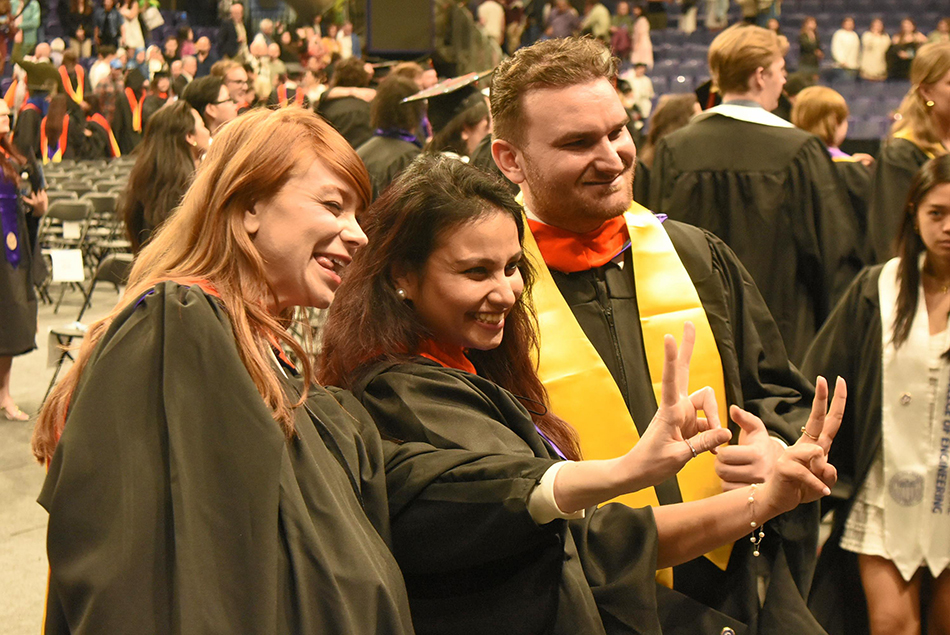 Three graduates taking a selfie and making hand gestures.