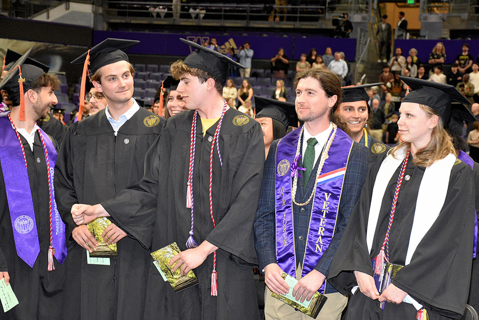 Group of graduates standing and chatting, holding diplomas.