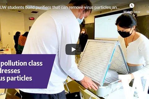 A screenshot of a video that shows two students attaching air filters on a fan