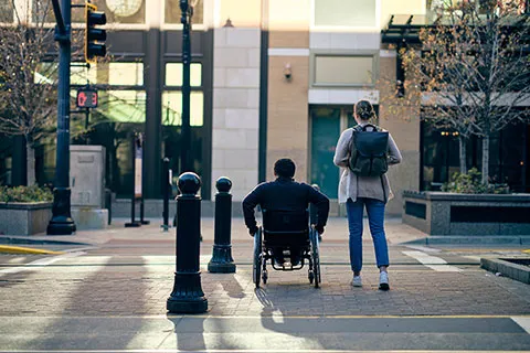 A person in wheelchair and another standing person at a city sidewalk