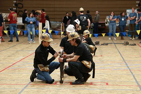 Students wearing hard hats building components of a steel bridge