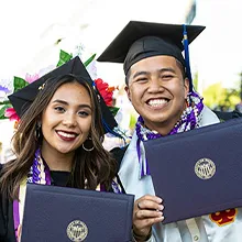 Two people, holding diplomas, are smiling at the camera.