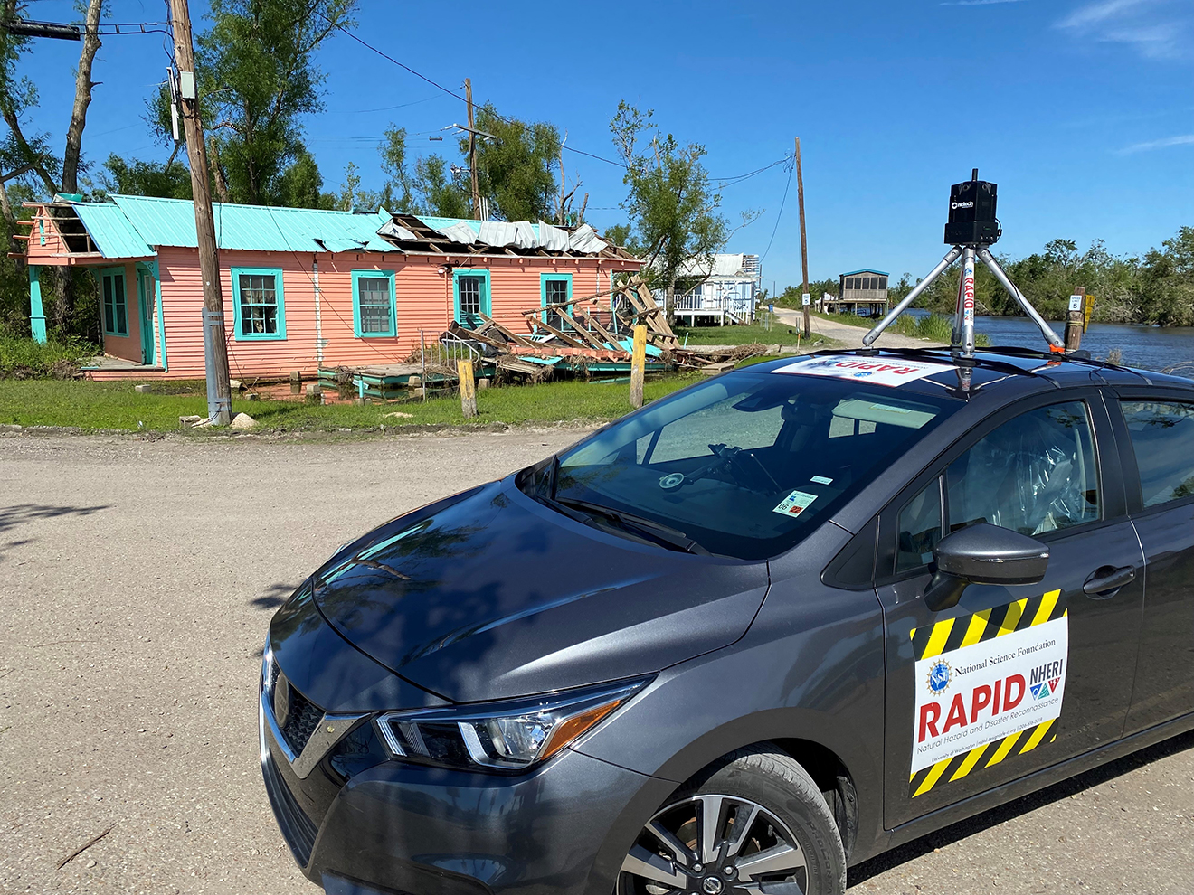 A car with a RAPID sign parked in front of a hurricane-damaged building